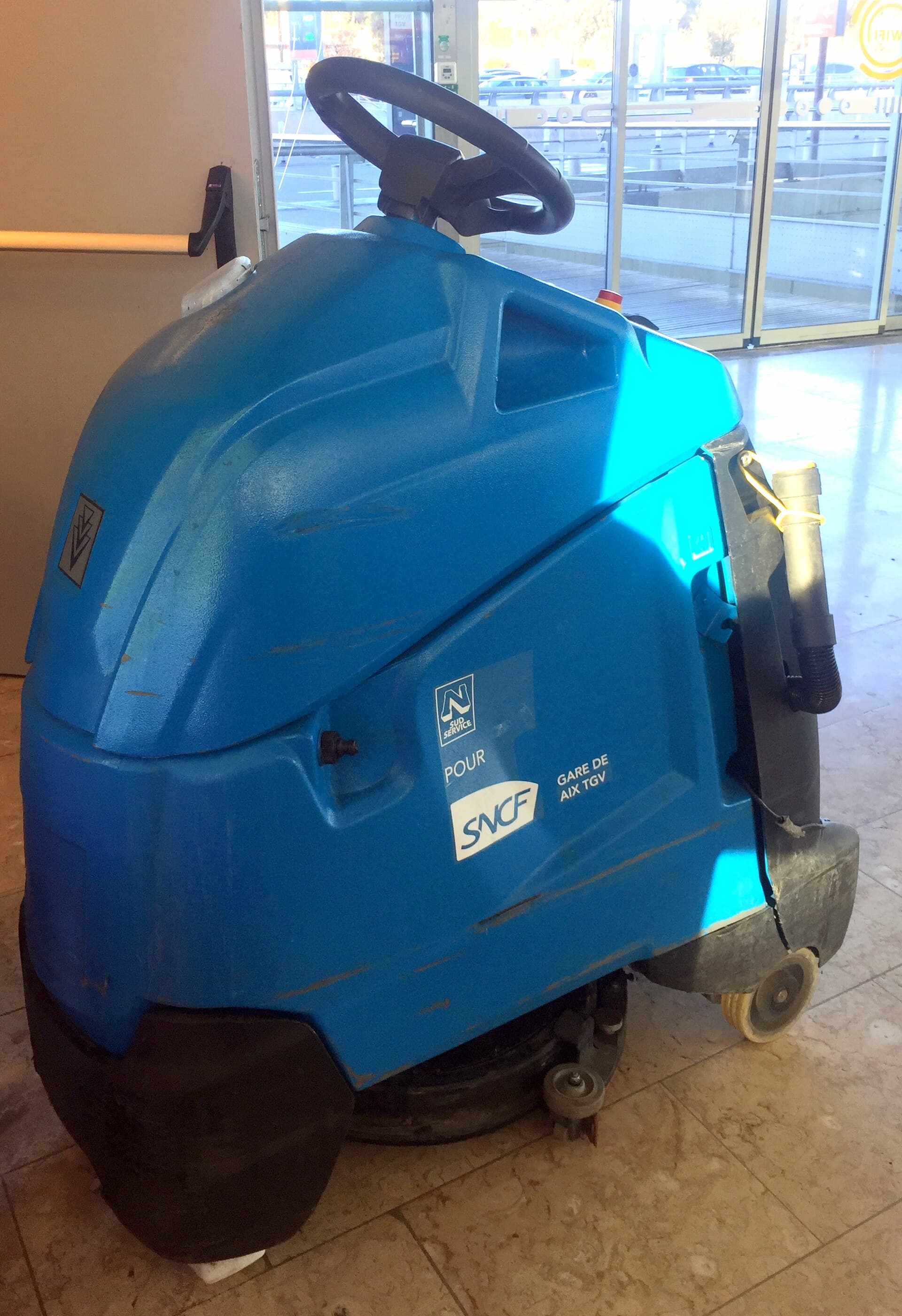 A walk-behind scrubber-dryer on a tiled concourse